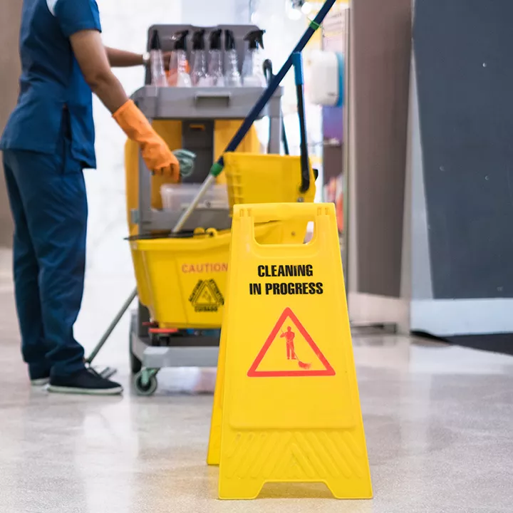 Janitor Cleaning Floor In Front Of Yellow Caution "Cleaning in progress". Cleaning service in public area.